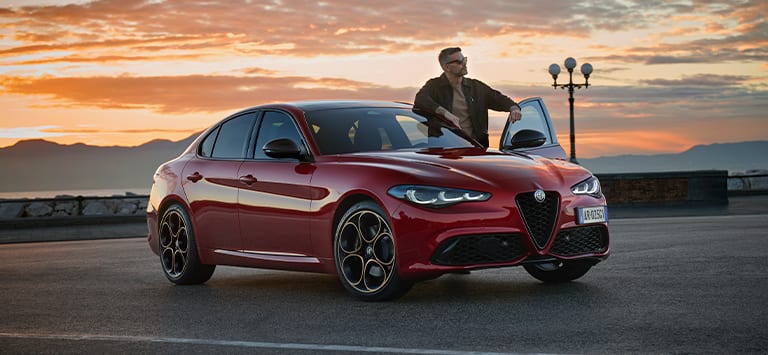 A European version red 2025 Alfa Romeo Giulia Intensa with the sunset over mountains in the background.
