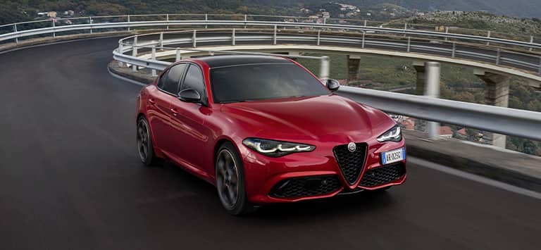 A European version red 2025 Alfa Romeo Giulia Intensa traveling on a curved bridge.
