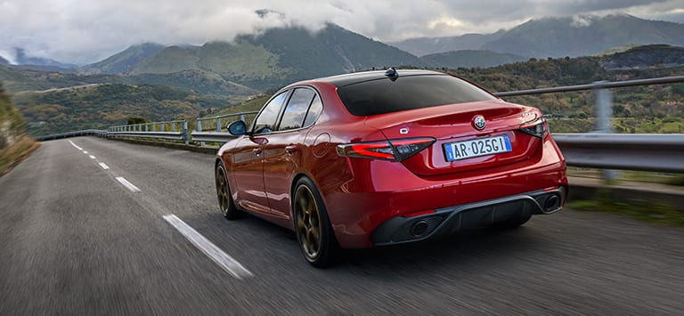 A rear angle of a European version red 2025 Alfa Romeo Giulia Intensa traveling on a mountain highway.