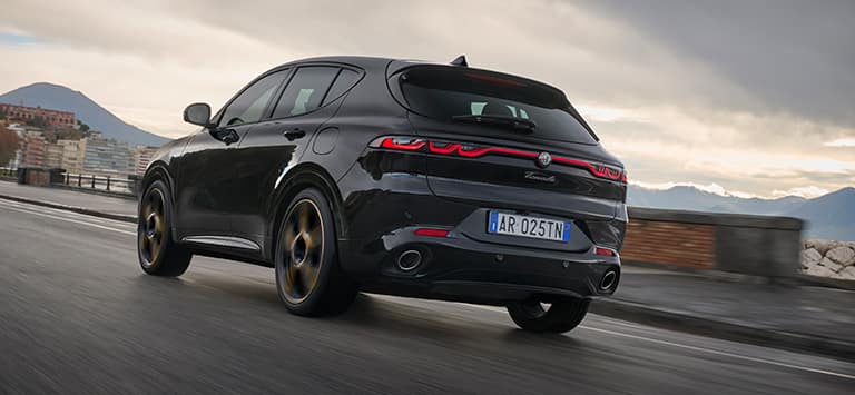 A rear angle of a European version black 2025 Alfa Romeo Tonale Intensa traveling on a highway.