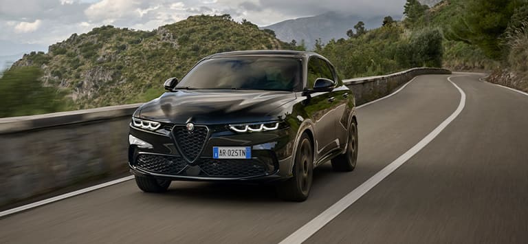A front angle of a European version black 2025 Alfa Romeo Tonale Intensa traveling on a highway in the mountains.