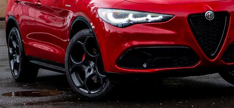 Parte inferior de la parte delantera y lado del pasajero de un Alfa Romeo Giulia Veloce 2026 rojo, incluidos con los neumáticos de las ruedas, mientras circula con lluvia.
