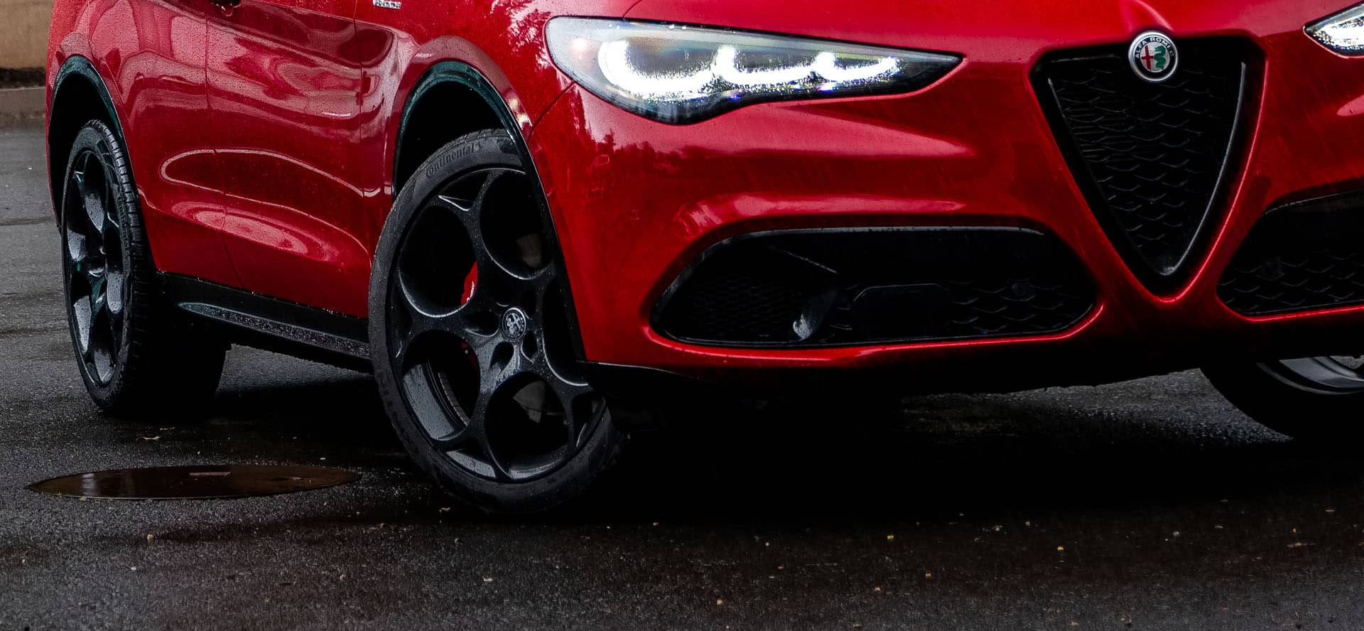 2026 Alfa Romeo Giulia front wheel and grille detail on a wet road, showcasing available Q4 all-wheel drive