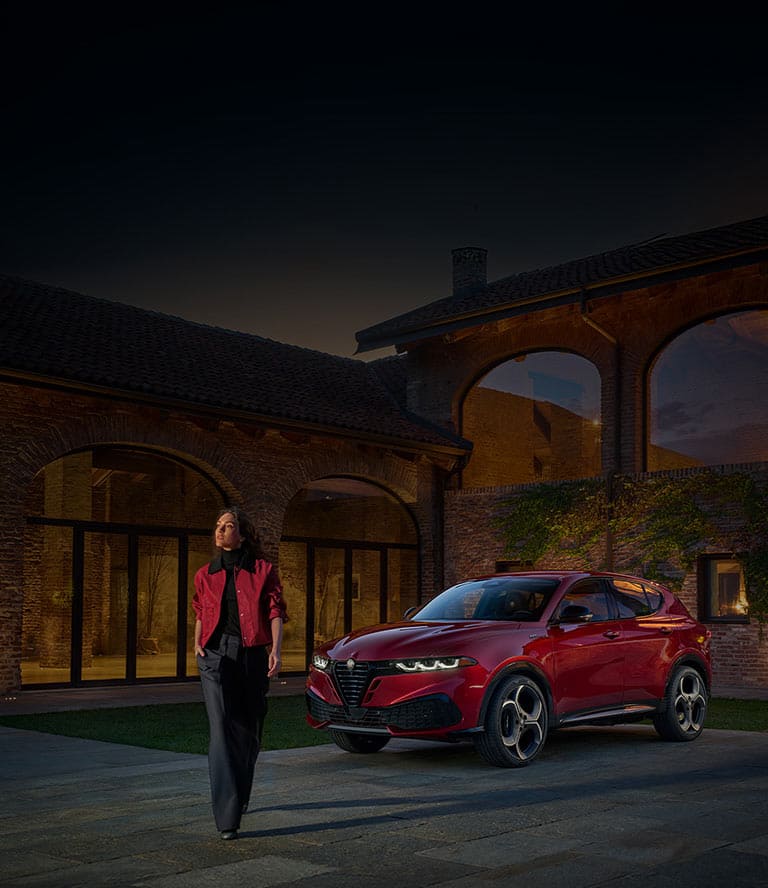 A red 2026 Alfa Romeo Tonale Sport Speciale model parked in a courtyard with a woman walking away from the vehicle