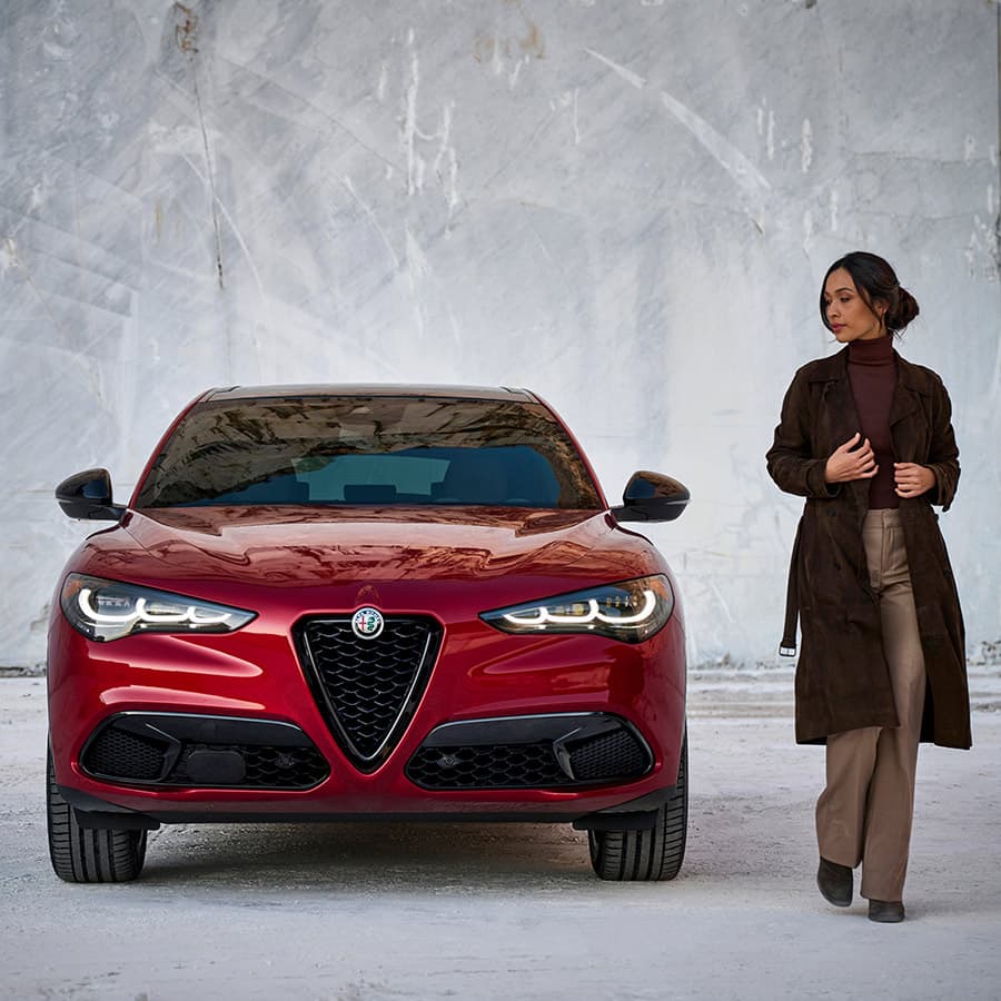 Vista trasera de un Alfa Romeo Giulia Veloce 2022 blanco estacionado en la arcada de un complejo de departamentos con una mujer caminando hacia el asiento del acompañante.