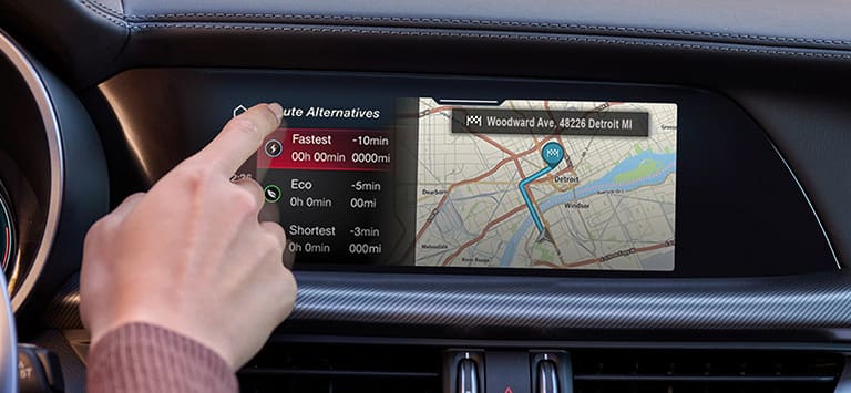 La pantalla táctil de Uconnect y las aberturas de calefacción y ventilación de un Alfa Romeo Stelvio 2026, con el conductor tocando la pantalla.