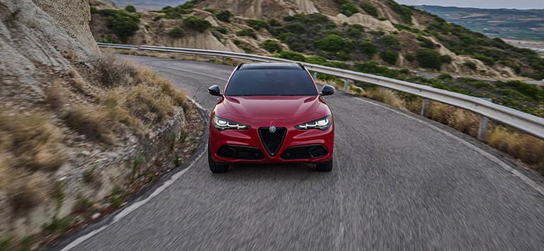 Un Alfa Romeo Stelvio Veloce 2026 rojo circulando por un camino de montaña sinuoso.