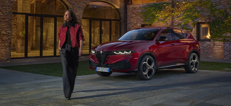 A red 2026 Alfa Romeo Tonale Sport Speciale parked in a courtyard with a woman walking away from the vehicle.