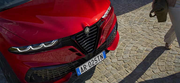 A raised angle of the front end of a red 2026 Alfa Romeo Tonale Sport Speciale focusing on the V Scudetto grille.