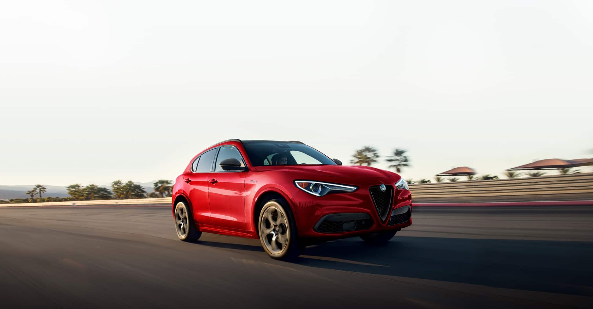 A three-quarter front view of the 2022 Stelvio being driven on a racetrack with palm trees in the background.