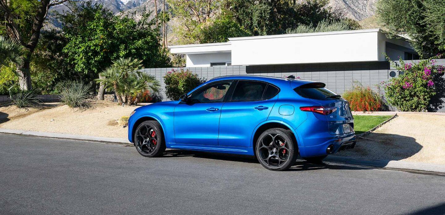 Display A profile view of a blue 2023 Alfa Romeo Stelvio Veloce parked on the street in front of a contemporary home.