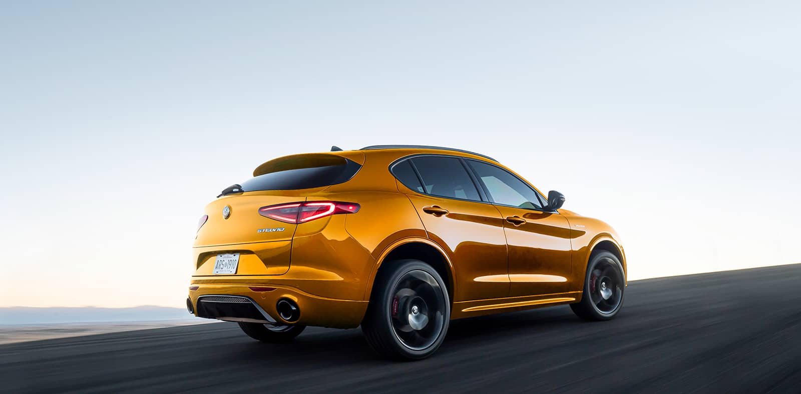 A three-quarter rear view of a gold 2023 Alfa Romeo Stelvio Veloce being driven on a highway.