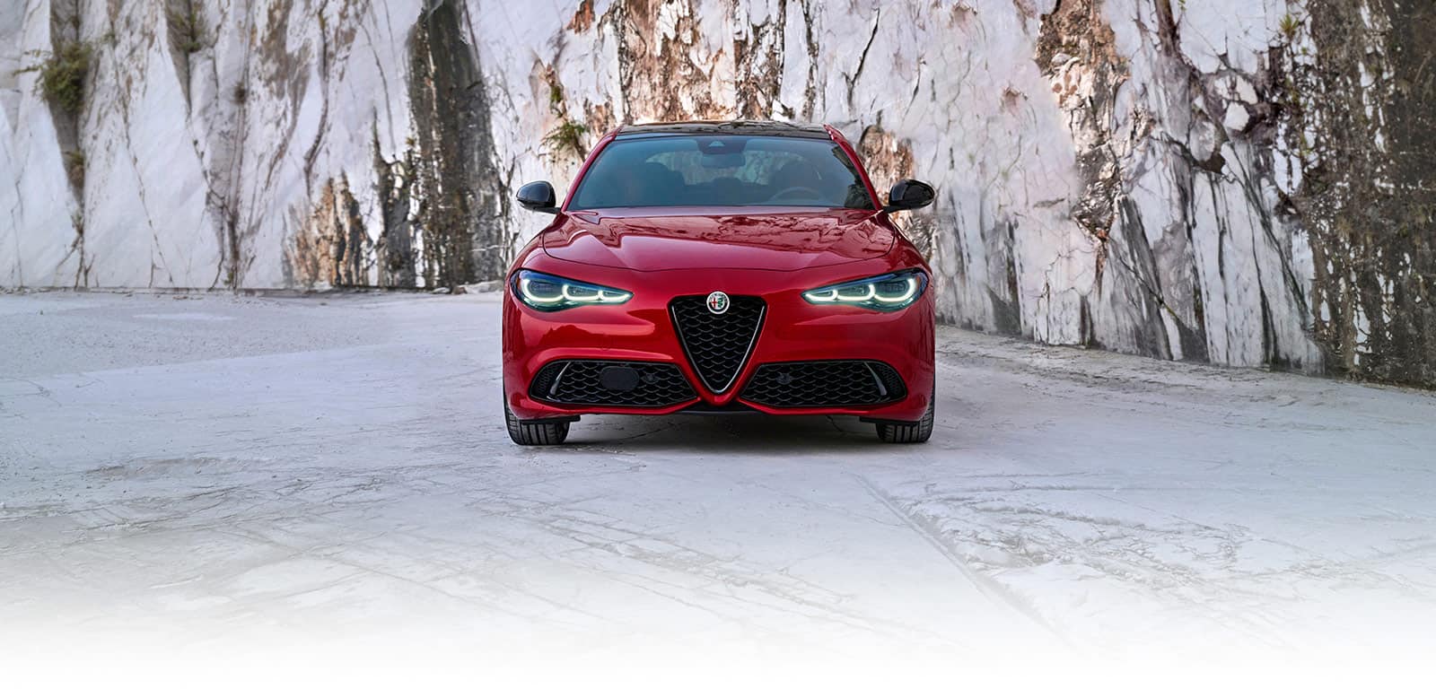 A head-on angle of a red 2024 Alfa Romeo Giulia parked in front of a wall of stone.