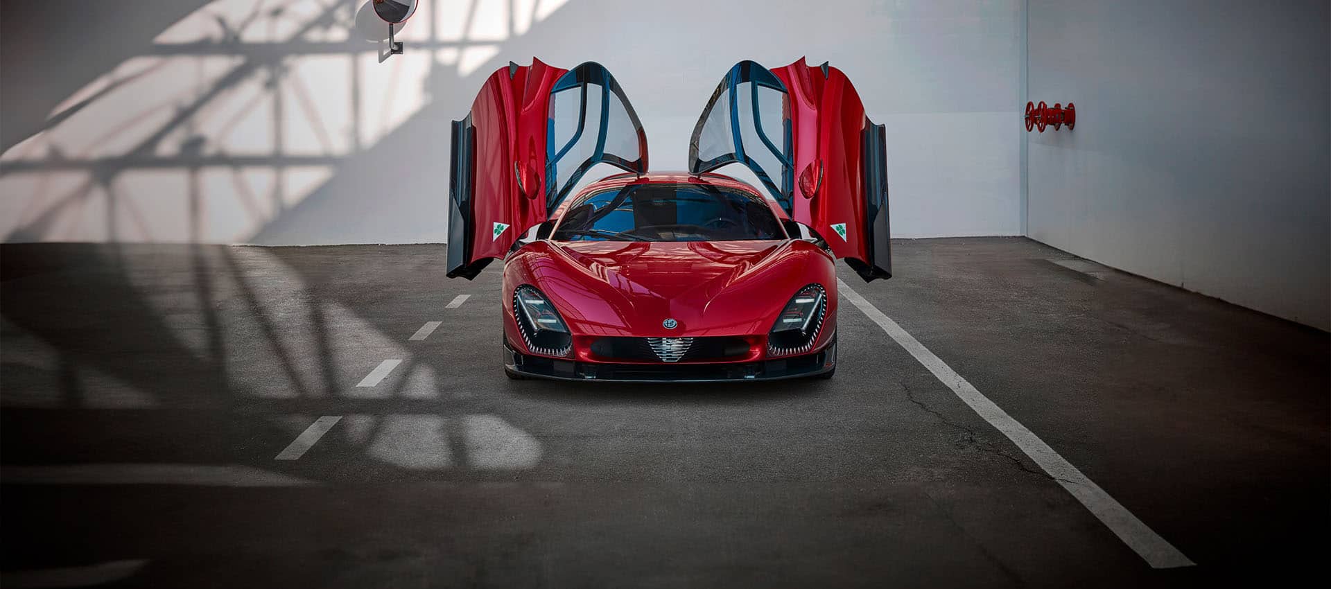 A head on view of a red 2025 Alfa Romeo 33 Stradale with its "elytra" doors open, parked in a commercial garage.