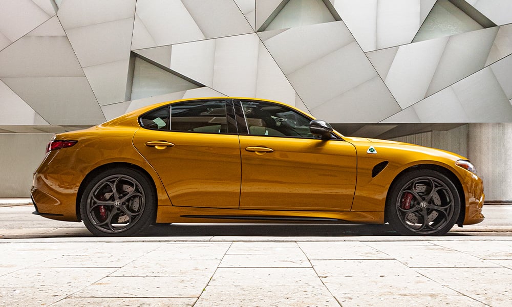  A profile view of a golden 2023 Alfa Romeo Giulia Quadrifoglio parked inside a building with an abstract design on the wall.