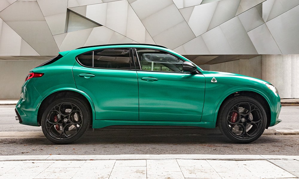 A profile view of a green 2023 Alfa Romeo Stelvio Quadrifoglio parked inside a building with an abstract design on the wall.